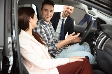 Salesman consulting young couple in auto at dealership. Buying new car