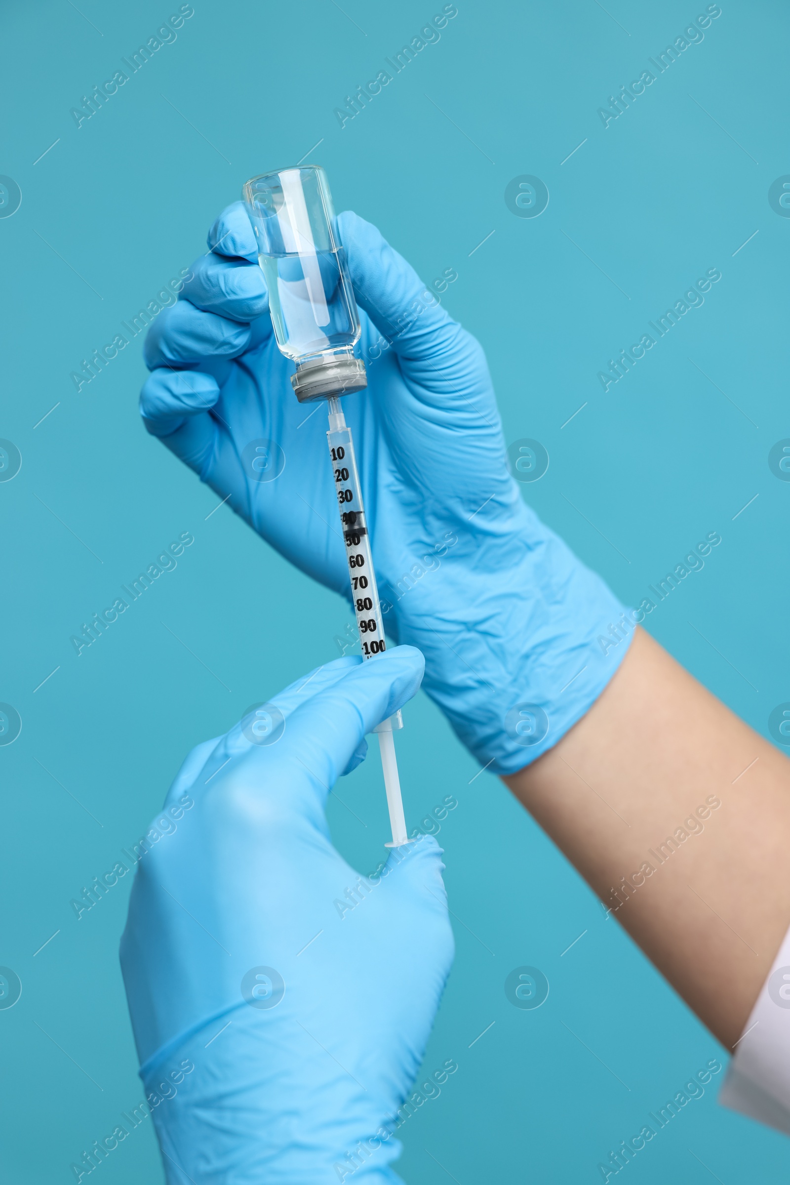 Photo of Doctor filling syringe with medication from glass vial on light blue background, closeup