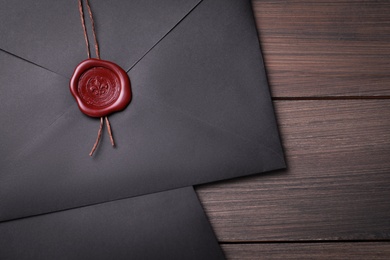 Photo of Black envelopes with wax seal on wooden background, flat lay