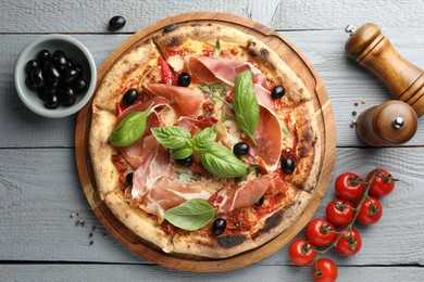 Photo of Tasty pizza with cured ham, olives, tomatoes and basil on gray wooden table, flat lay