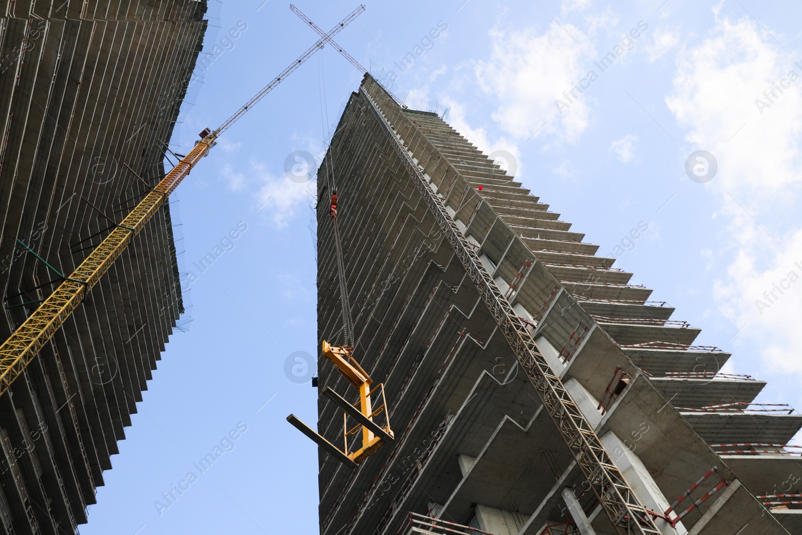 Photo of Tower crane near unfinished buildings against cloudy sky on construction site, low angle view