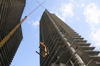 Photo of Tower crane near unfinished buildings against cloudy sky on construction site, low angle view