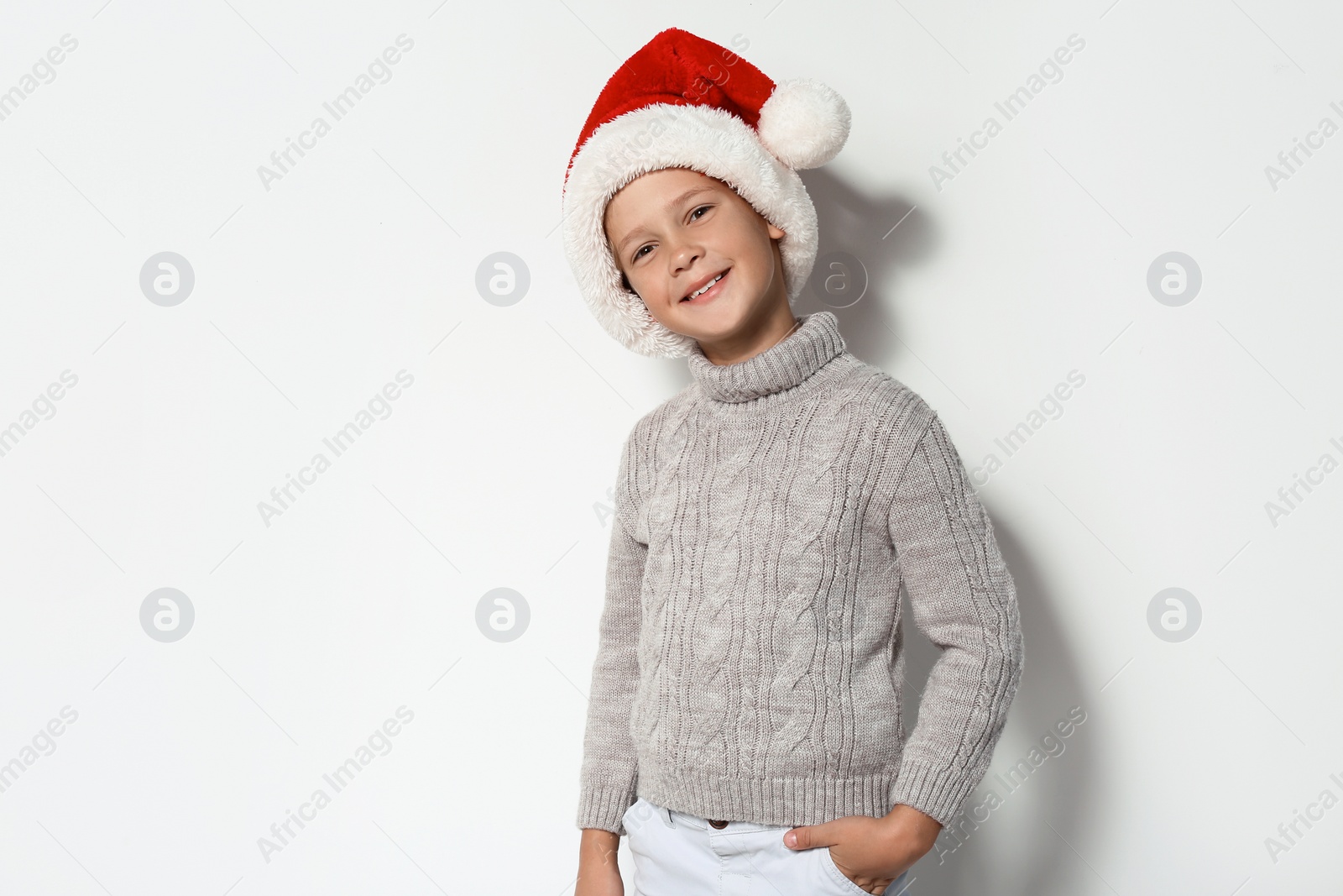 Photo of Cute little boy in warm sweater and Christmas hat on white background