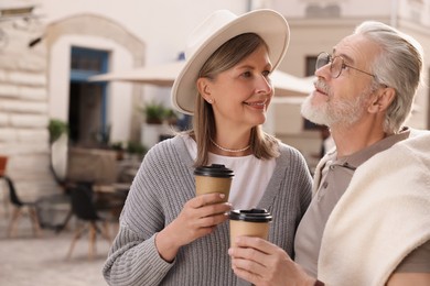 Affectionate senior couple with coffee walking outdoors, space for text