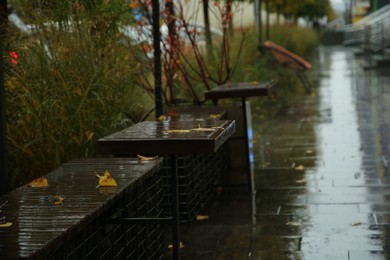 Photo of Wet tables and benches on city street after rain