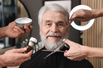 Photo of Professional barbers taking care of client's mustache and beard in barbershop