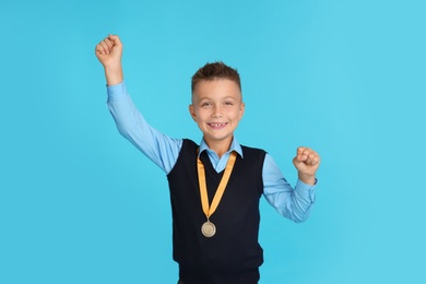 Happy boy in school uniform with golden medal on blue background