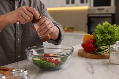 Cooking process. Man adding salt into bowl of salad at white marble countertop kitchen, closeup