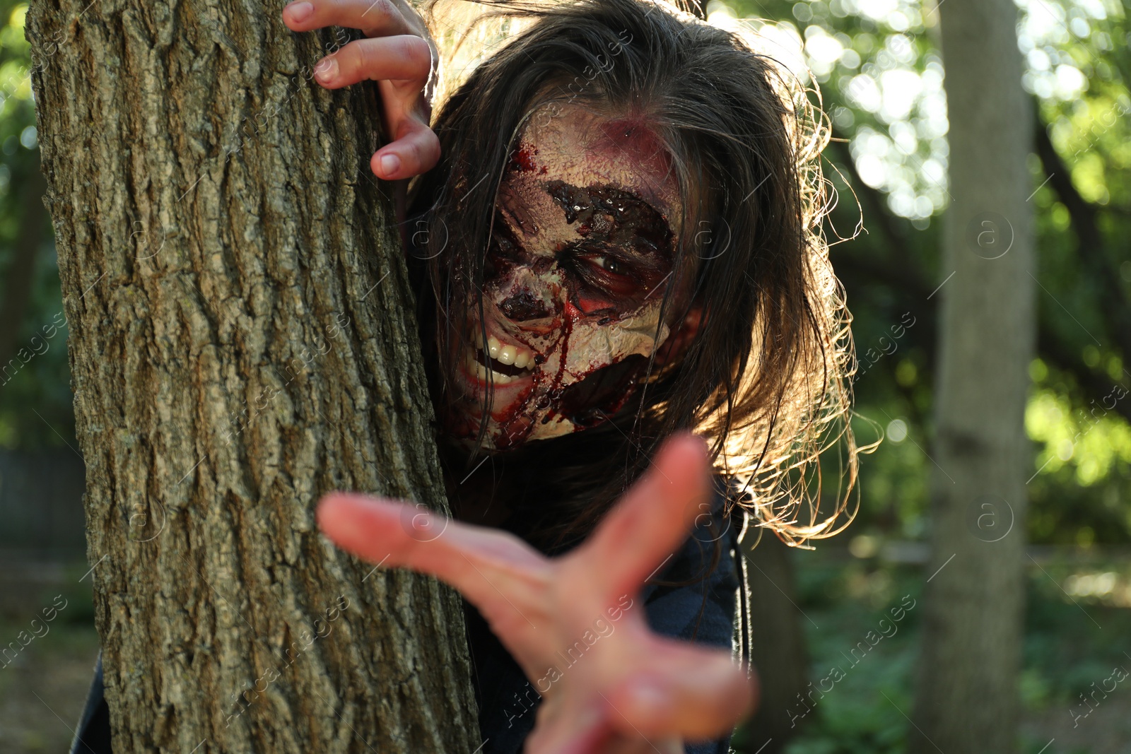 Photo of Scary zombie near tree outdoors. Halloween monster