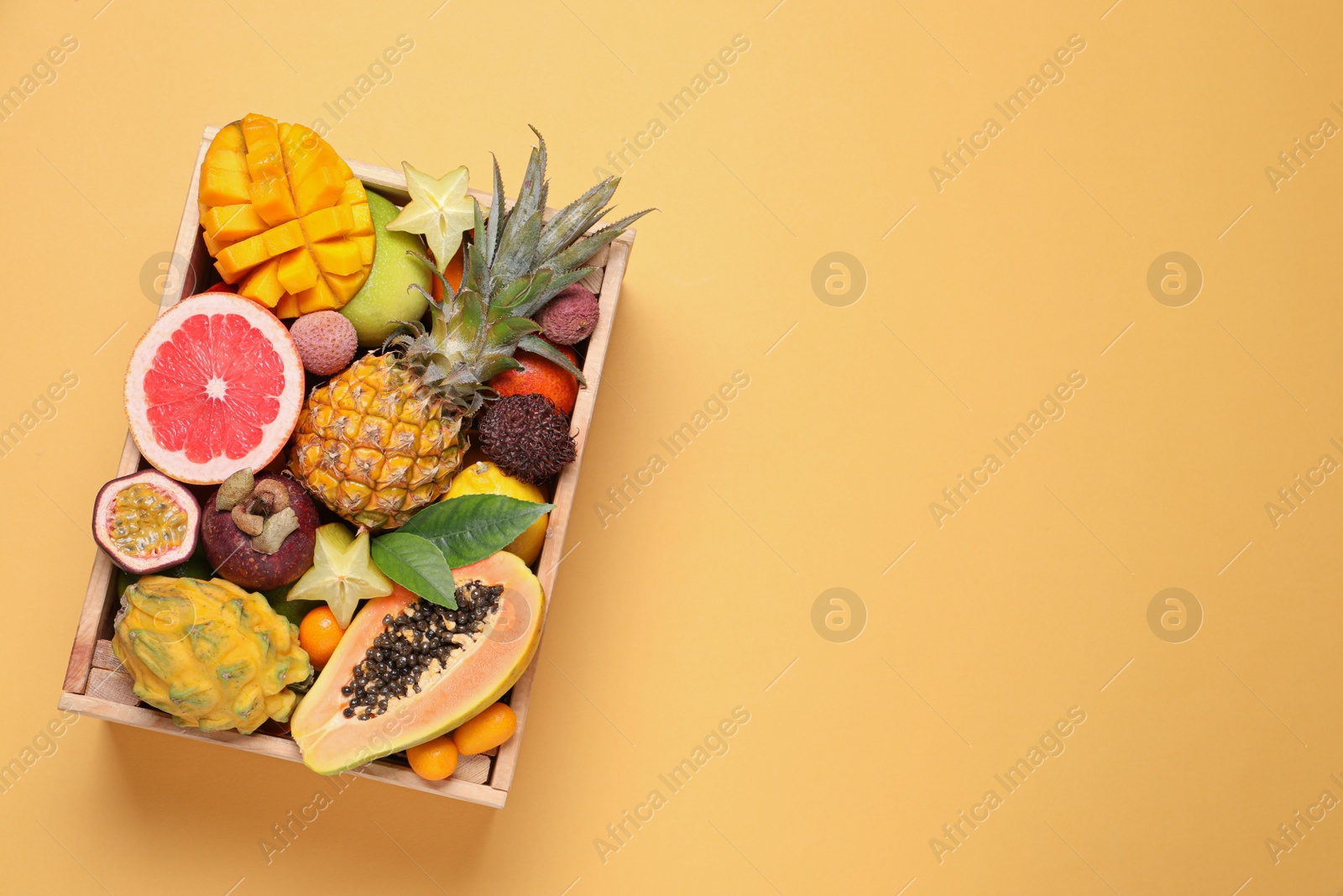 Photo of Crate with different exotic fruits on yellow background, top view. Space for text