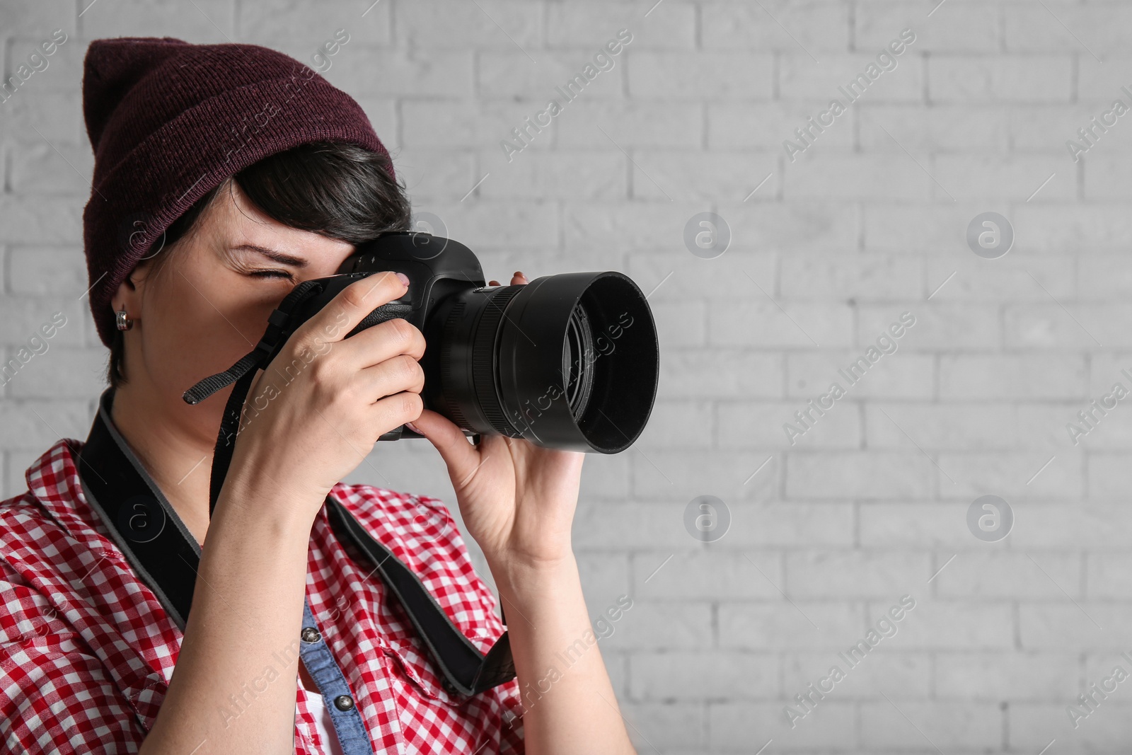 Photo of Young female photographer with camera on brick background