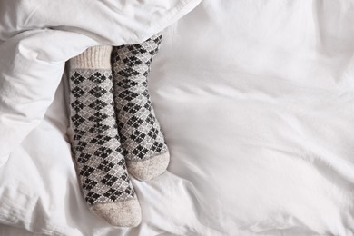 Woman wearing knitted socks under blanket in bed, top view. Space for text