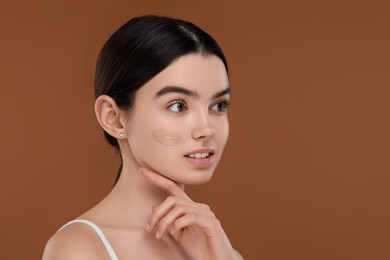 Photo of Teenage girl with swatch of foundation on face against brown background. Space for text