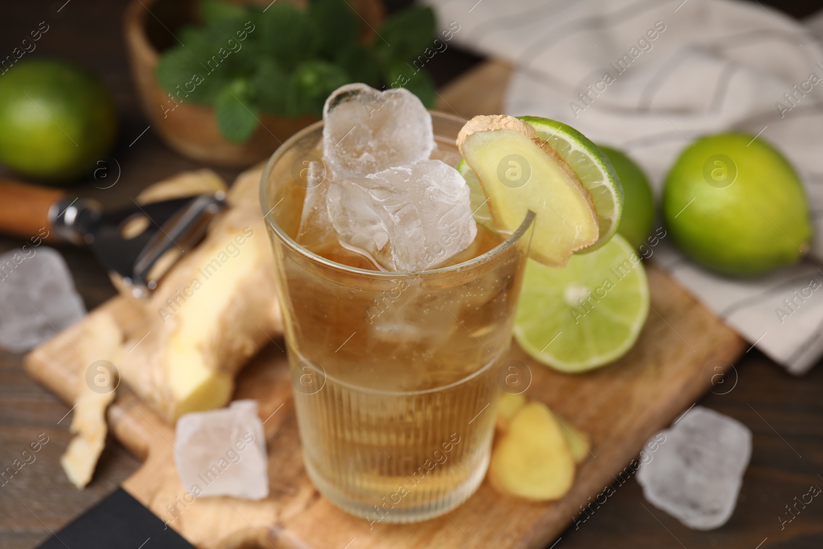 Photo of Glass of tasty ginger ale with ice cubes and ingredients on wooden table, closeup