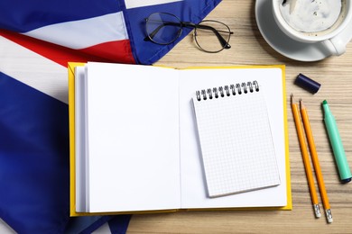 Photo of Learning foreign language. Open book, flag of United Kingdom, stationery and glasses on wooden table, flat lay