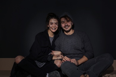 Photo of Poor young couple sitting on floor near dark wall