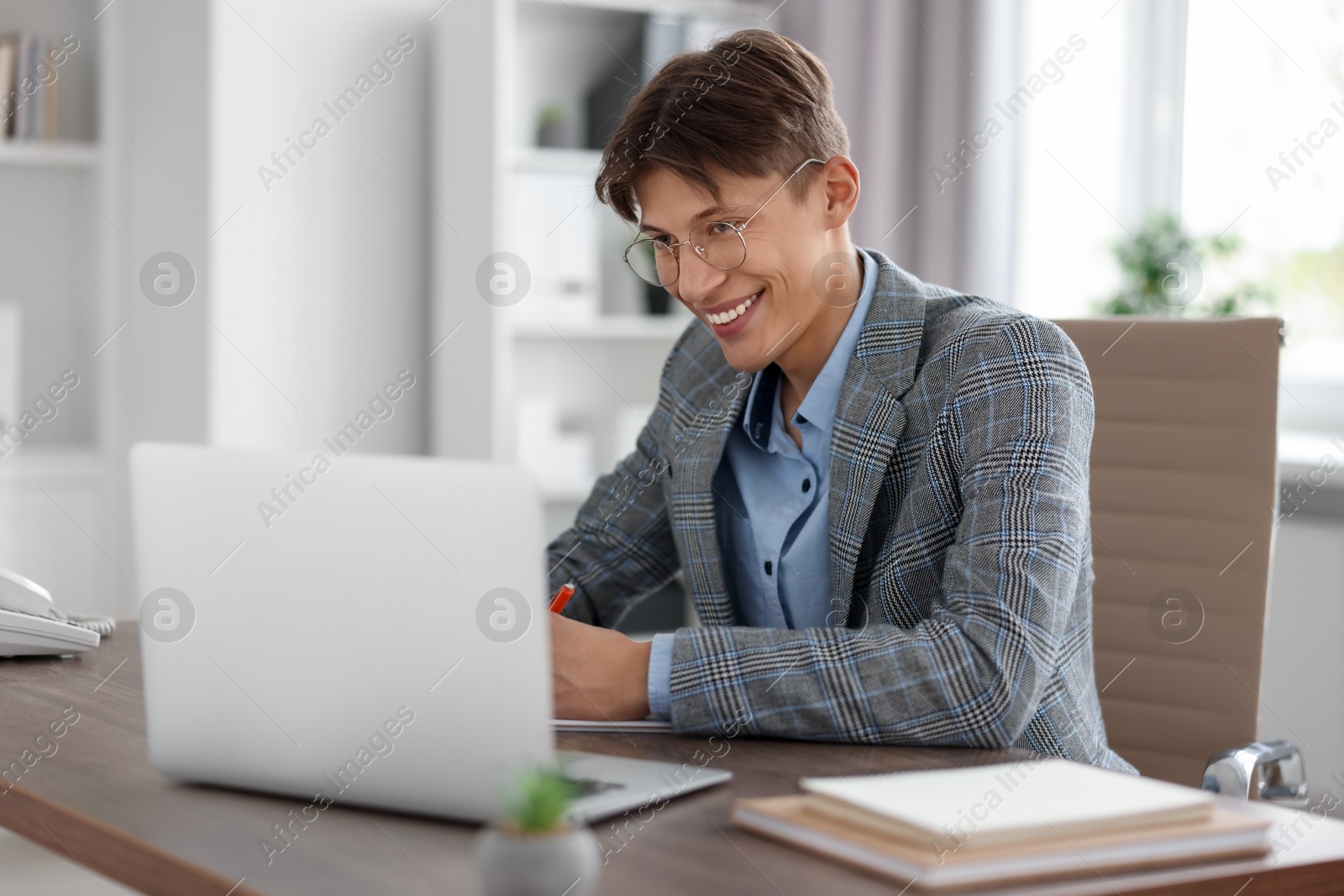 Photo of Man taking notes during webinar at wooden table in office