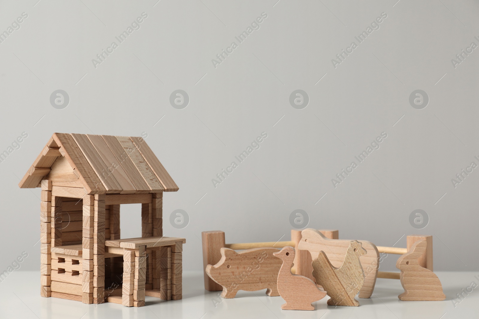 Photo of Wooden house, animals and fence on white table near light grey wall. Children's toys