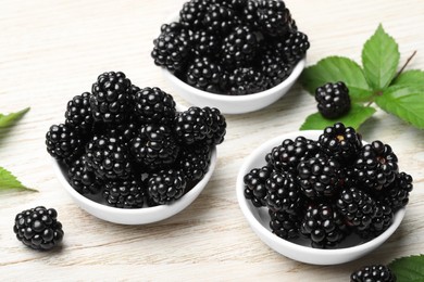 Photo of Ripe blackberries and green leaves on white wooden table, closeup