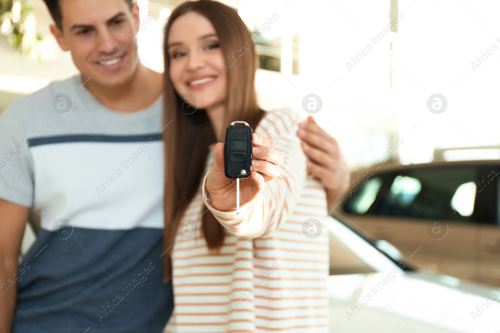 Photo of Happy couple with car key in modern auto dealership, focus on hand