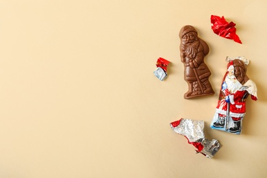 Photo of Flat lay composition with chocolate Santa Claus candies on beige background, space for text