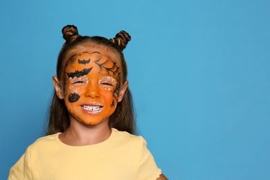 Photo of Cute little girl with face painting on blue background. Space for text