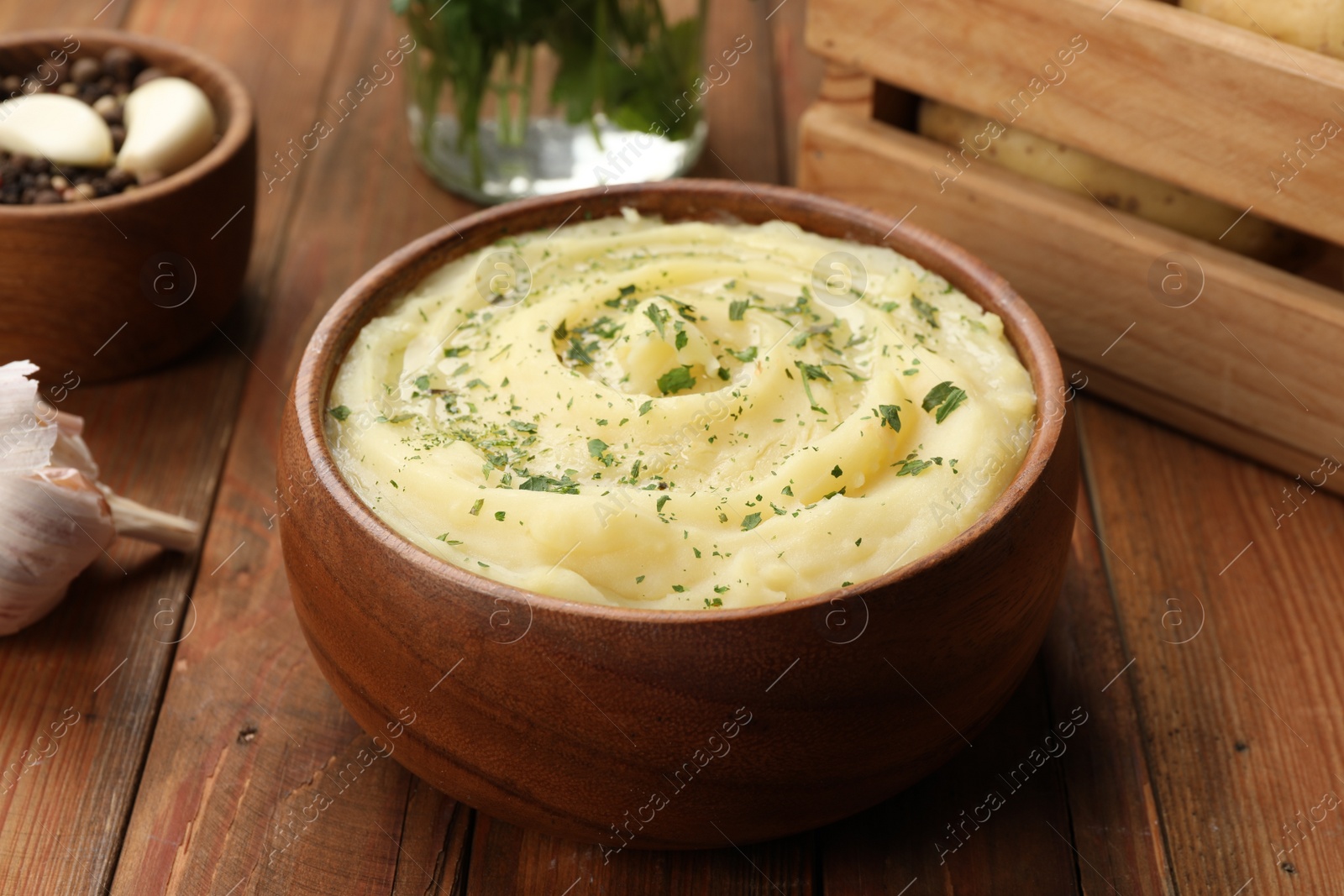 Photo of Bowl of tasty mashed potato with greens, garlic and pepper on wooden table, closeup