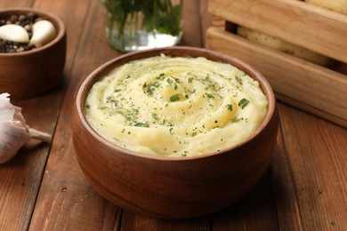 Photo of Bowl of tasty mashed potato with greens, garlic and pepper on wooden table, closeup