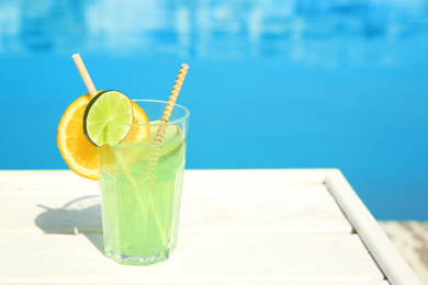 Photo of Refreshing cocktail near outdoor swimming pool on sunny day. Space for text