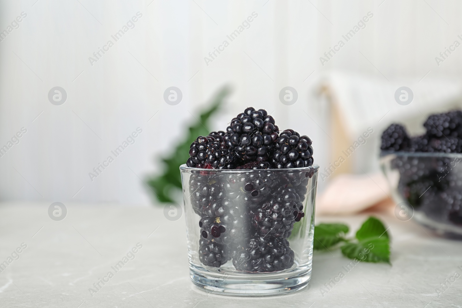 Photo of Glass with fresh blackberry on table against blurred background