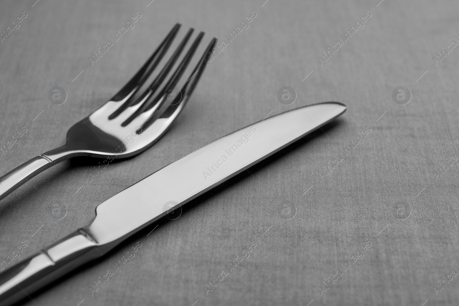 Photo of Shiny fork and knife on grey table, closeup