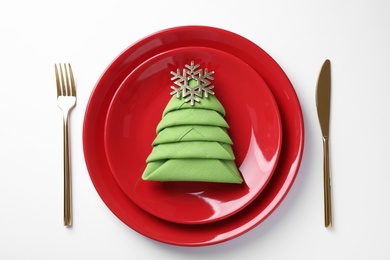 Festive table setting with green napkin folded in shape of Christmas tree on white background, top view
