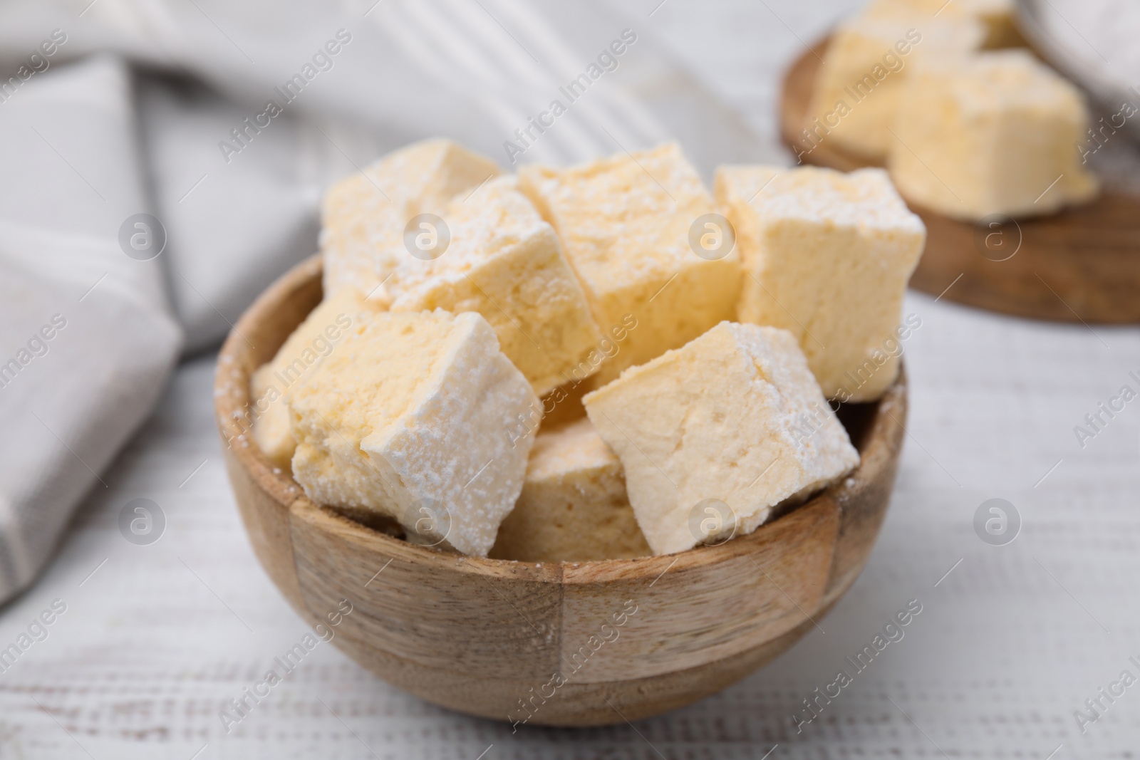 Photo of Bowl with tasty marshmallows on white wooden table, closeup