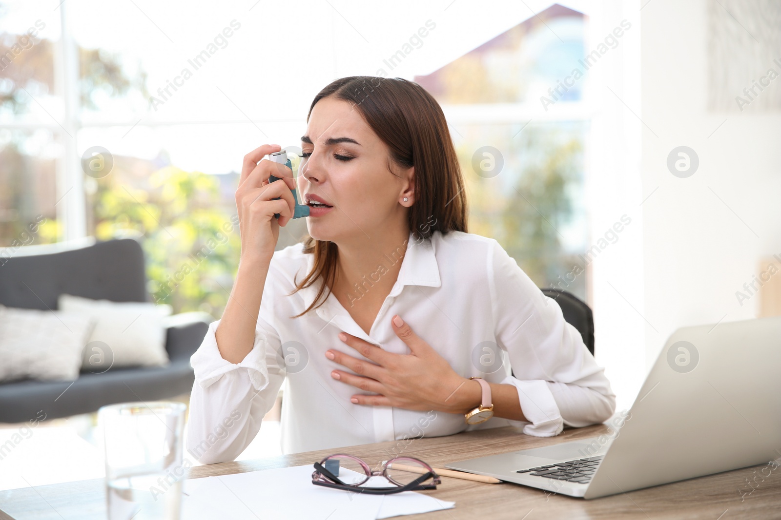 Photo of Young woman with asthma inhaler at table in light room