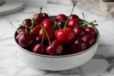 Fresh ripe cherries with water drops in bowl on white marble table, closeup