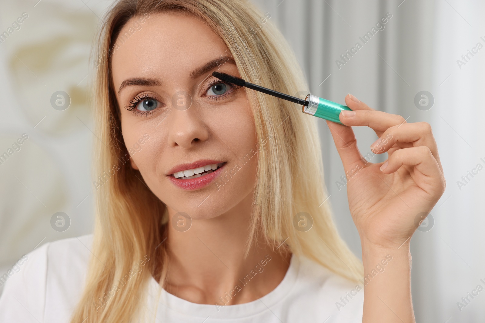 Photo of Beautiful woman applying mascara with brush indoors, closeup