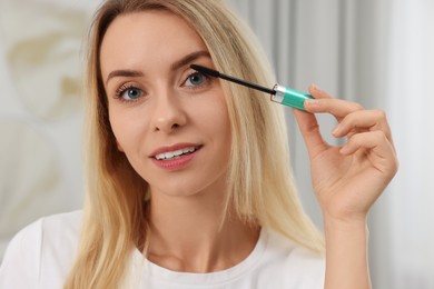 Photo of Beautiful woman applying mascara with brush indoors, closeup