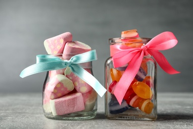 Photo of Tasty sweets in glass jars on light grey table, closeup