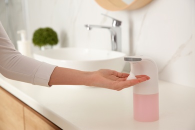 Woman using automatic soap dispenser in bathroom, closeup