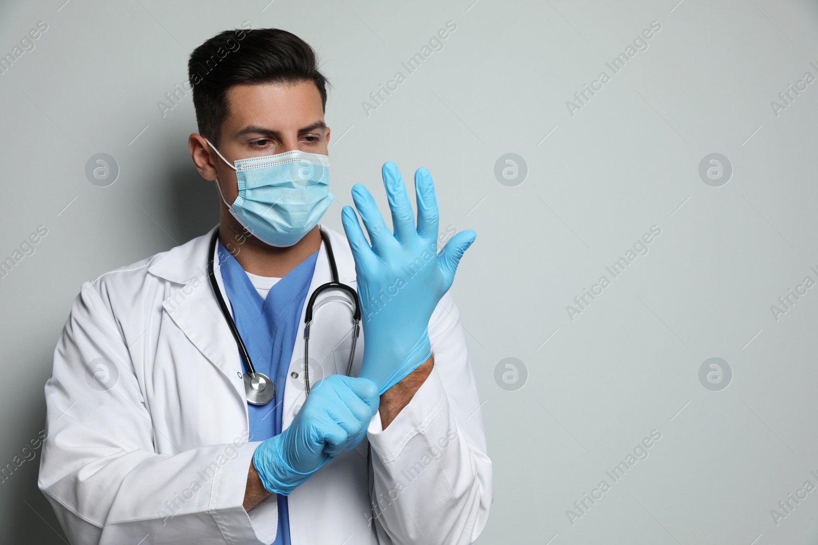 Photo of Doctor in protective mask putting on medical gloves against light grey background