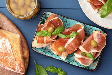 Photo of Tasty sandwiches with cured ham and basil leaves on blue wooden table, flat lay