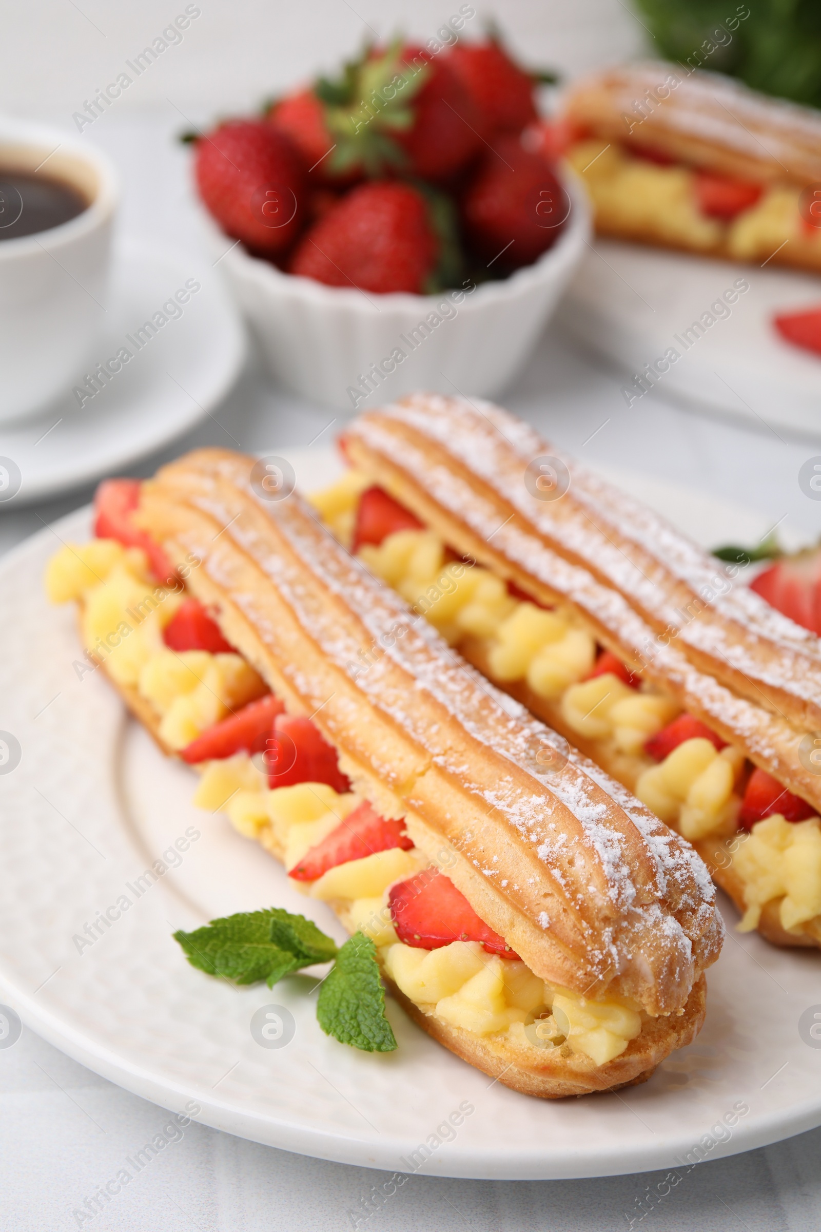 Photo of Delicious eclairs filled with cream, strawberries and mint on table, closeup