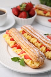 Delicious eclairs filled with cream, strawberries and mint on table, closeup