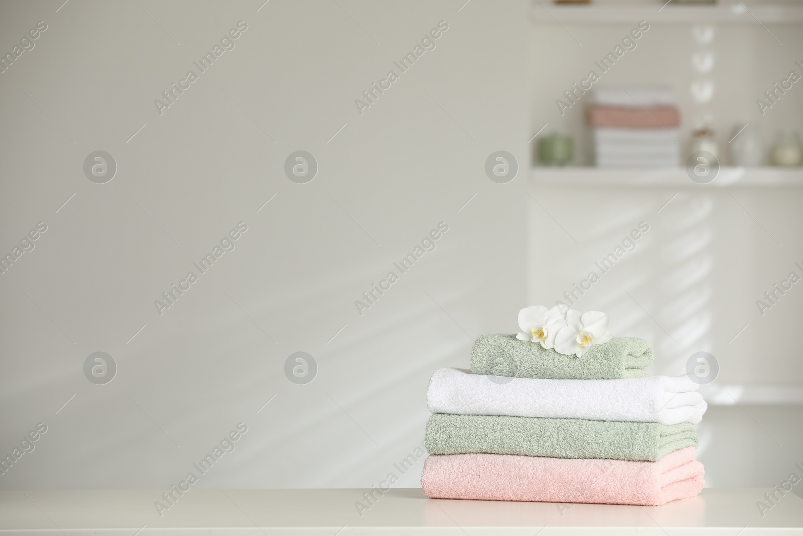 Photo of Stack of clean soft towels with orchid flowers on white table indoors. Space for text