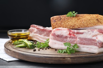 Pieces of raw pork belly, chili pepper, peppercorns, oil and parsley on black wooden table, closeup