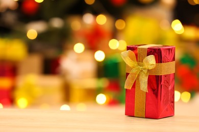 Photo of Beautifully wrapped gift box on wooden table against blurred festive lights, space for text. Christmas celebration