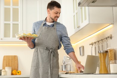 Man making dinner while watching online cooking course via laptop in kitchen