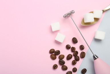 Pink milk frother wand, coffee beans and sugar cubes on color background, flat lay. Space for text