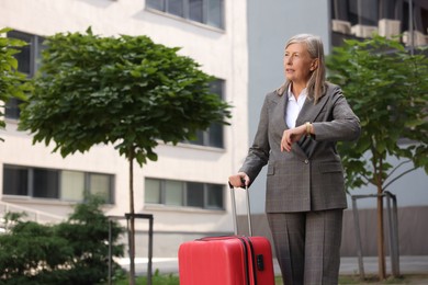 Photo of Being late. Worried senior businesswoman with red suitcase outdoors