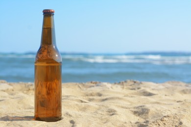 Photo of Bottle of beer on sandy beach near sea. Space for text